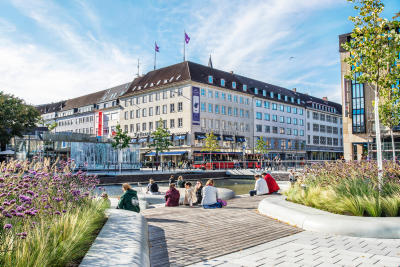 Ein belebter Platz am Holstenfleet in Kiel, mit Menschen, Gebäuden und urbaner Landschaft.